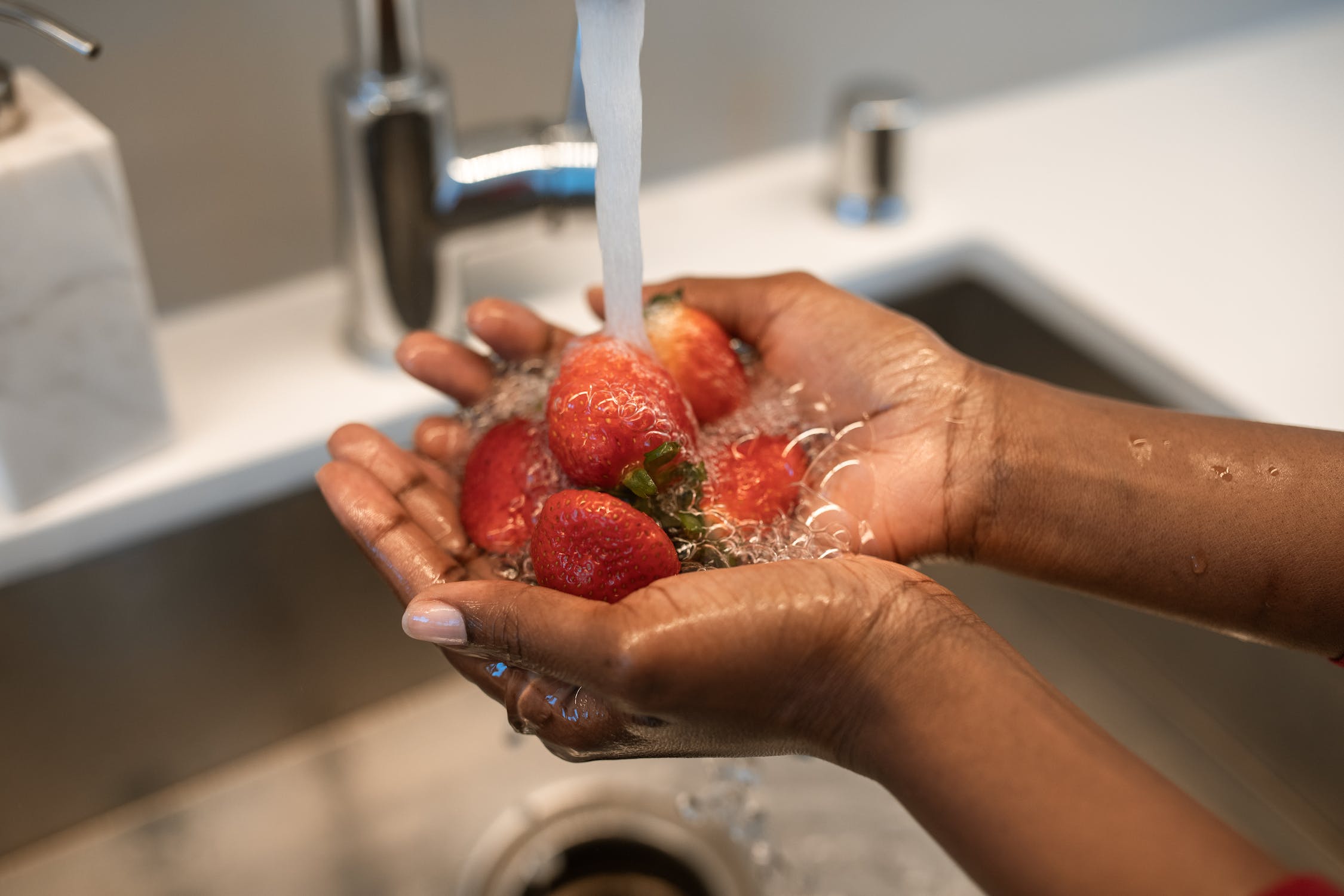 A person washing strawberries under a faucet
