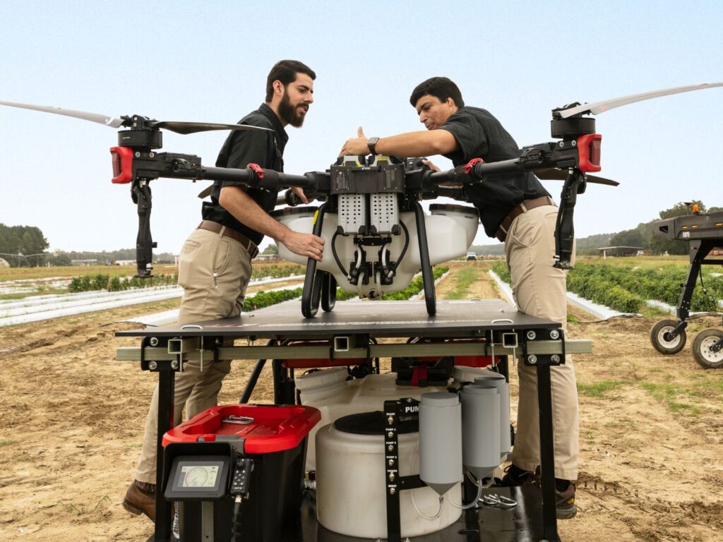 Two scientists in an agricultural field working on a drone sitting on a large dock.